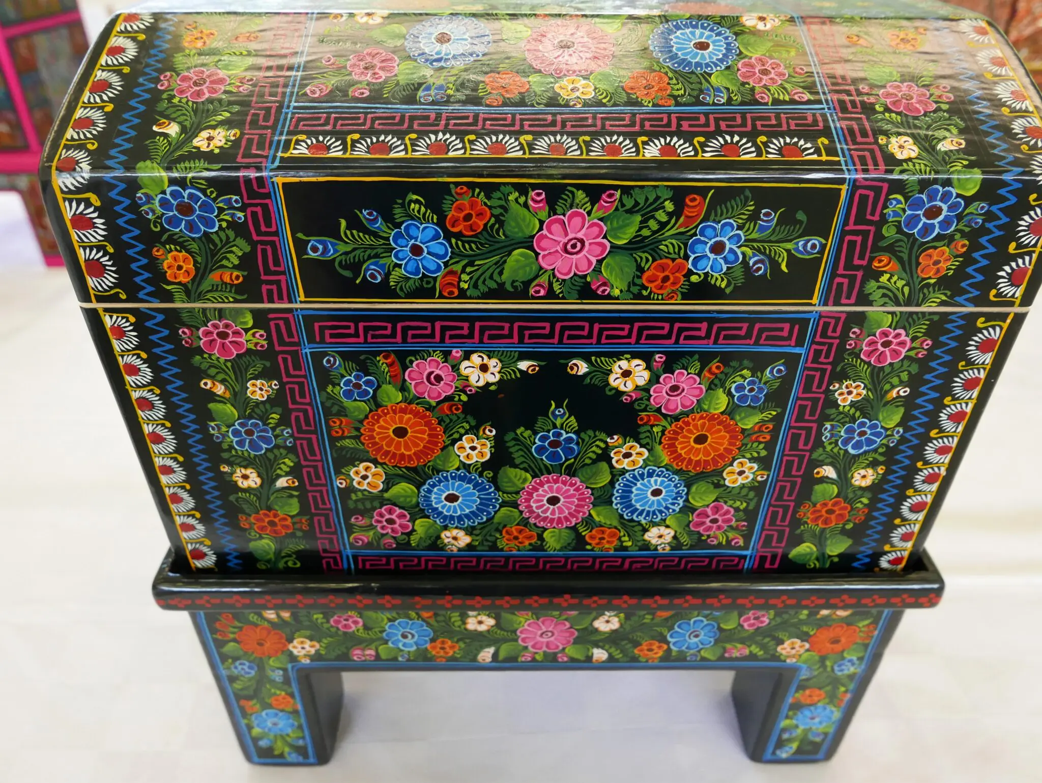 Black wooden chest with intricate hand-painted floral designs on it, sitting atop a white floor