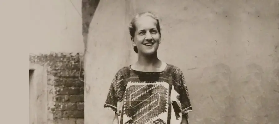 Black and white photo of a woman standing in front of a wall, She is wearing a dress