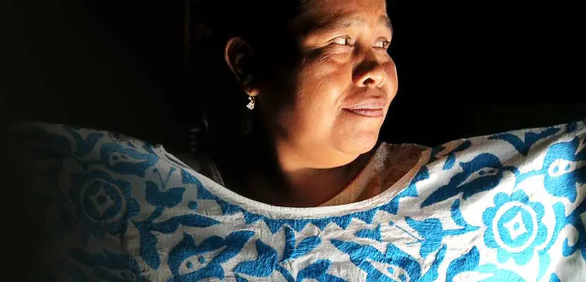 Woman in a blue and dress sitting in a dark room, looking up at the sky
