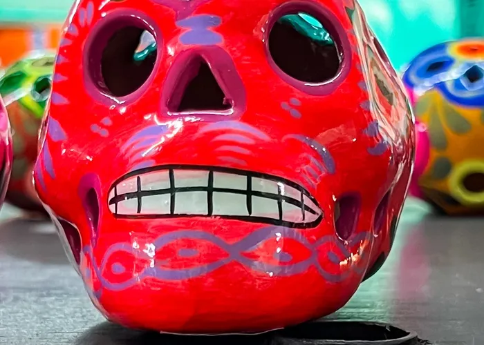 Red skull sitting atop a table, surrounded by colorful Day of the Dead skulls