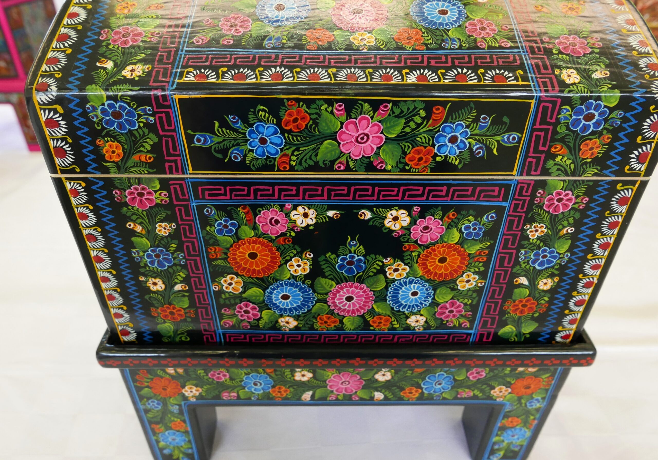 Black wooden chest with intricate hand-painted floral designs on it, sitting atop a white floor