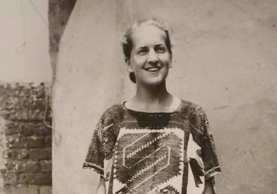 Black and white photo of a woman standing in front of a wall, She is wearing a dress