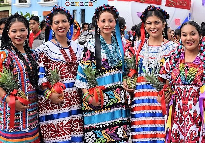Group of women in colorful dresses standing next to each other, and holding pineapples in their hands